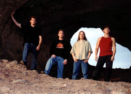 GROUNDED: four members framed in a desert rock arch