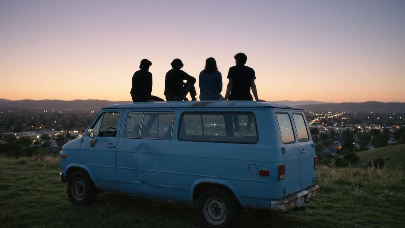 Four silhouettes on the roof of a blue van above a city at dusk